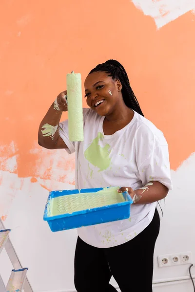 Yeni dairesinde duvar boyayan güzel bir Afrikalı Amerikalı kadın. Yenileme ve dekorasyon konsepti. — Stok fotoğraf