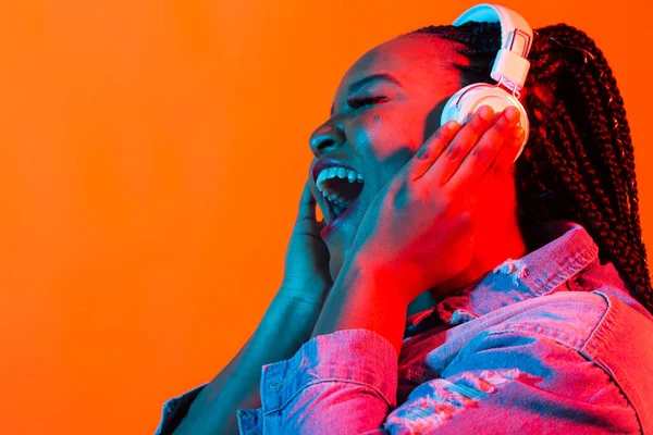 Jovem afro-americana ouvindo música em fones de ouvido em luz de néon. Retrato feminino. Conceito de emoções humanas, expressão facial, feriados ou fim de semana, hobby , — Fotografia de Stock