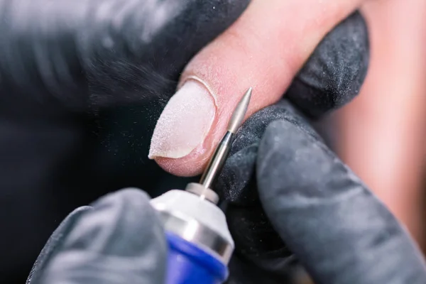 Manicure hardware in un salone di bellezza. manicure femminile sta applicando trapano lima elettrica per unghie per manicure sulle dita femminili. Manicure meccanica primo piano. Concetto cura del corpo. — Foto Stock