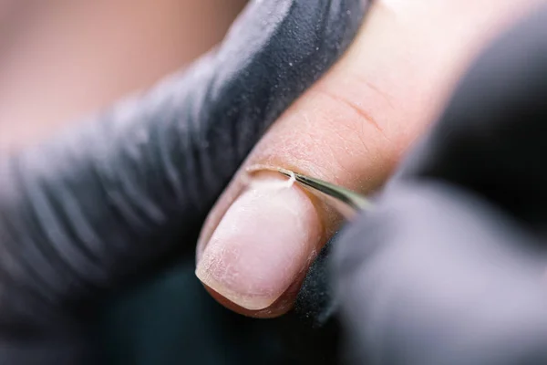 Primo piano mani estetiste professionali che lavorano con trapano elettrico sulle unghie del cliente. Procedura di applicazione unghie artificiali. Mani di manicure con strumento. Manicurista in guanti rimuove cuticola — Foto Stock