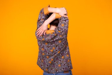 Evde siyah saçlı heyecanlı genç bir kadın pijama giyiyor, gülümsüyor ve eğleniyor. Sarı arka planda izole edilmiş. Arka plan.