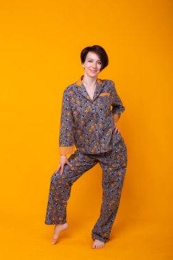 Evdeki neşeli kadın pijama stüdyosu tarzı sarı arka plan duyguları giyiyor..