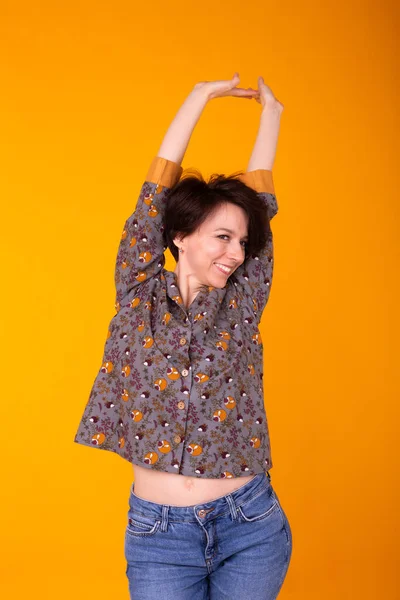 Aufgeregte junge Frau im Pyjama, weithin lächelnd, Spaß habend. Vereinzelt auf gelbem Hintergrund. — Stockfoto