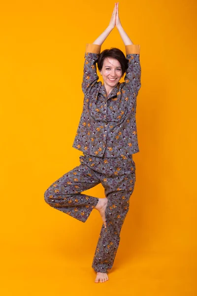 Mujer joven emocionada con el pelo negro en el pijama de uso doméstico, ampliamente sonriendo divertirse. Aislado sobre fondo amarillo. Concepto de yoga . — Foto de Stock
