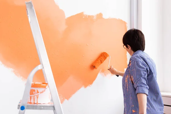 Yeni evde orta yaşlı mutlu bir kadın boya rulosuyla duvarları boyuyor. Duvara boya süren tekerlekli sandalyeli bir kadın.. — Stok fotoğraf