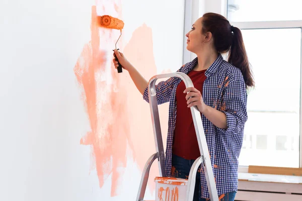 Bella donna sorridente pittura parete interna della casa con rullo di vernice. Ristrutturazione, ristrutturazione, riparazione di appartamenti e concetto di ristoro. — Foto Stock
