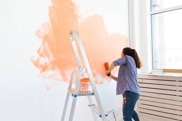 Glad ung kvinna målar interiör vägg med färg roller i nytt hus. En kvinna med roller applicera färg på en vägg. — Stockfoto
