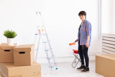 Yenileme, dekorasyon ve onarım konsepti - orta yaşlı kadın yeni evinde duvar boyuyor.