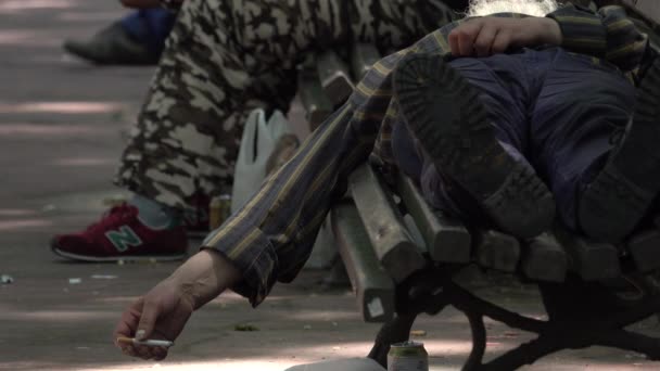 Hajléktalan férfi egy nyilvános parkban dohányzás — Stock videók