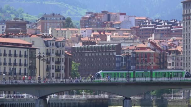 Bilbao Tram atravessa a ponte com a cidade por trás — Vídeo de Stock