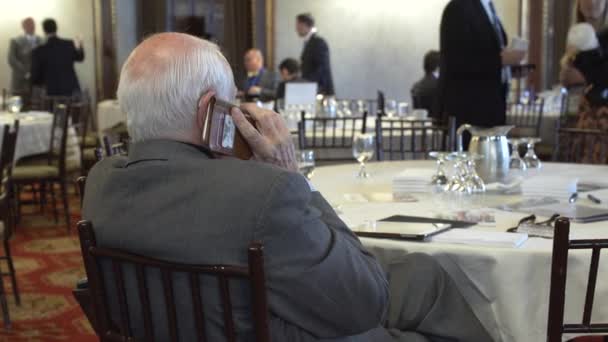 En äldre man använder telefonen i en matsal — Stockvideo