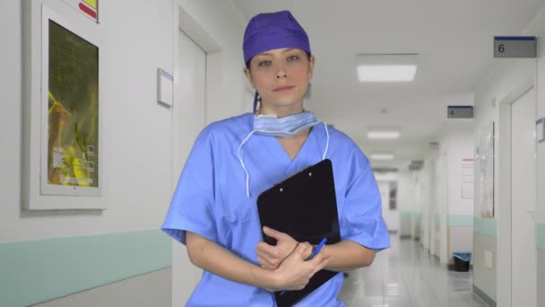 Серьезный хирург с кепкой и планшетом в коридоре больницы — стоковое видео