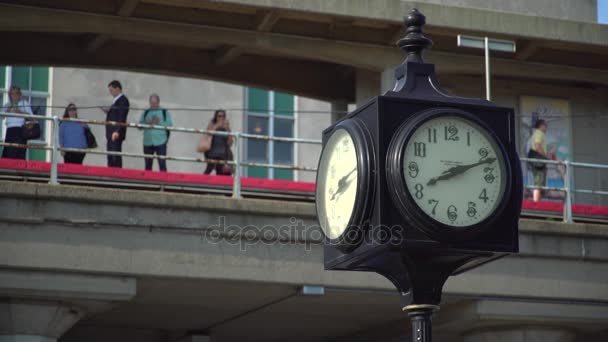 Klok op voorgrond met pendelaars die wachten op een treinstation — Stockvideo