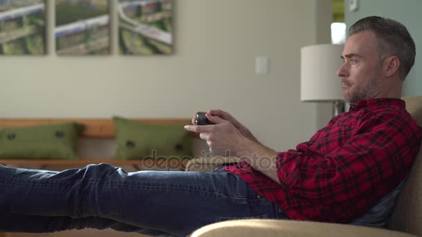Ο άνθρωπος με προσήλωση παίζοντας ένα παιχνίδι βίντεο σε έναν καναπέ — Αρχείο Βίντεο