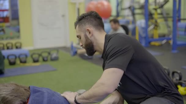 Мужской физический тренер помогает клиенту растянуться — стоковое видео