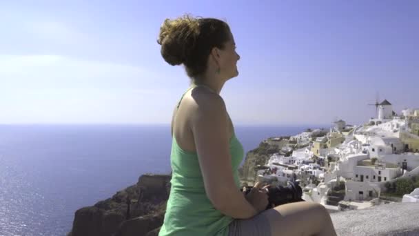 Pan to a woman on vacation photographing Oia — Stock Video