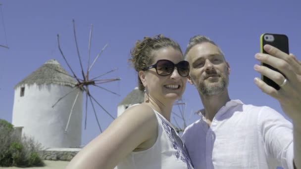 Una pareja se toma una selfie frente a los molinos de Mykonos — Vídeo de stock