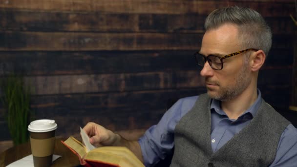 Man wearing vest reads with coffee nearby — Stock Video