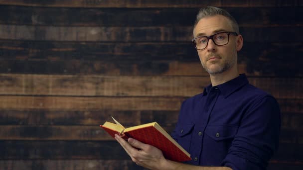 Hombre leyendo libro cruza brazos y sonríe — Vídeos de Stock