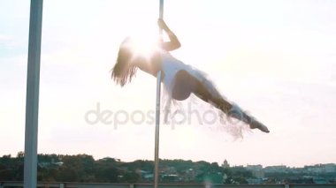 Seksi çekici kız poledancer gelişmiş kutup dans hileler taşınabilir dans sahnede gün batımında manzarası üzerinde gerçekleştirir.