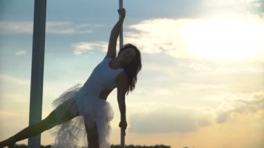 Seksi çekici kız poledancer gelişmiş kutup dans hileler taşınabilir dans sahnede gün batımında manzarası üzerinde gerçekleştirir.