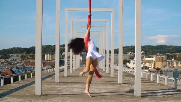 Hermosa bailarina en seda aérea. Joven mujer sexy realiza acrobacias en la azotea contra el cielo con nubes . — Vídeos de Stock