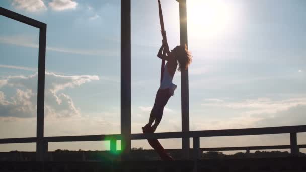 Bela dançarina em seda aérea. Jovem mulher sexy realiza acrobacias acrobáticas no telhado ao pôr do sol . — Vídeo de Stock