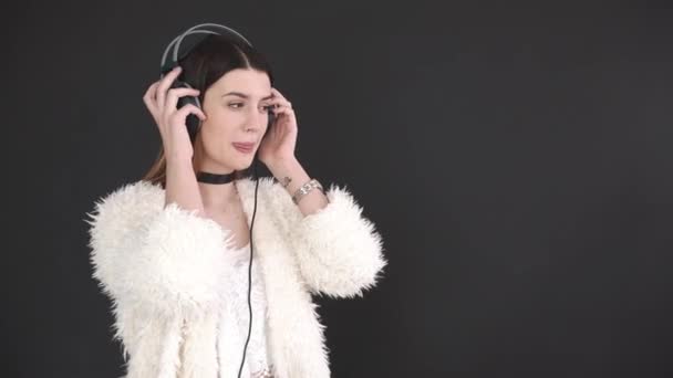 Roztomilá dívka poslouchá hudbu se sluchátky. Stojící na levé straně. na šedém pozadí, samostatný. — Stock video