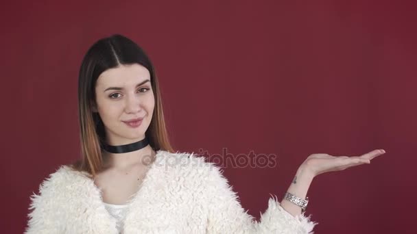 Menina sorridente feliz mostrando algo no fundo vermelho — Vídeo de Stock