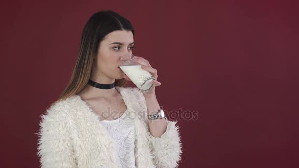 Mädchen trinkt ein Glas Milch auf dem roten Hintergrund. — Stockvideo