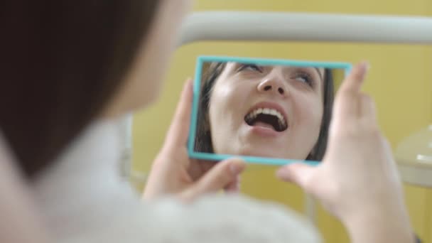 Jonge vrouwen in de tandarts stoel. De tandarts onderzoekt de mond. Mooie vrouw die lacht. Door het spiegel schot. — Stockvideo