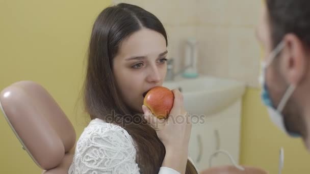 Porträtt av vackra unga kvinnan i stolen. Flicka äta ett äpple och tittar på kameran. Begreppet hälsa och ett vackert leende. — Stockvideo