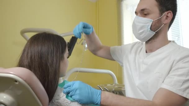 Dentista masculino se prepara para examinar uma paciente do sexo feminino na clínica odontológica, coloca no peito pano estéril . — Vídeo de Stock