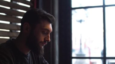 Genç içme kahve pencerenin kafede yanındaki adam. Bir sakallı bir adam