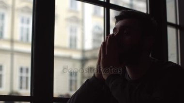 Pencere ve mesafe içine bakmak yakınındaki kafede oturan genç adam. Hes, kötü bir ruh halinde düşünceli. Yüz önünde tutan eller. Yakın çekim