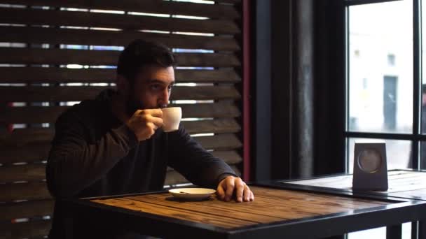 若い男のカフェでウィンドウの横にコーヒーを飲む。ひげを持つ男. — ストック動画