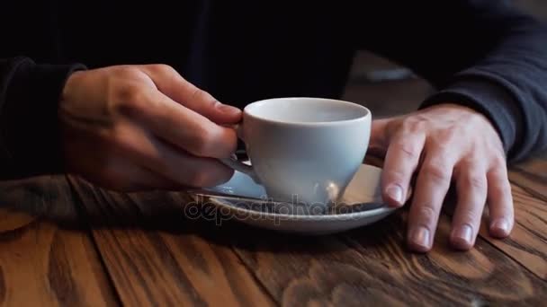 Sziluettjét a fiatal ember, aki mellett az ablak a kávézóban kávét iszik. Egy férfi szakáll. — Stock videók