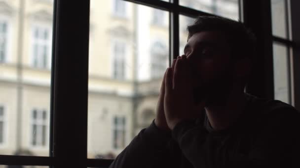 Jonge man zitten in Cafe in de buurt van venster en kijk in afstand. Hes broeden, in een slecht humeur. Bedrijf handen voor het gezicht. Close-up — Stockvideo