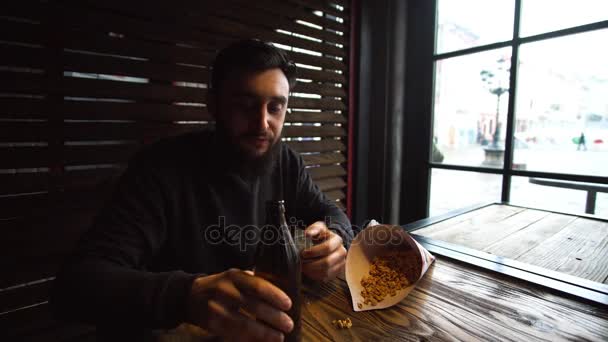 Jeune homme boire de la bière et manger des collations au bar près de la fenêtre . — Video