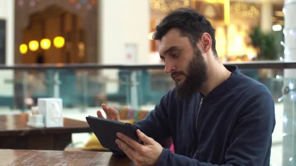 Νεαρός άνδρας με υπολογιστή δισκίο που κάθονται στο καφενείο — Αρχείο Βίντεο