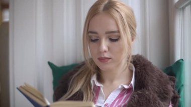 Bir kitap ve pencereden dışarı bakar kenarında oturan güzel genç kadın okuma