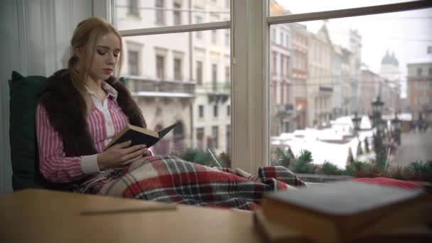 Mooie jonge vrouw zittend op de vensterbank en lezen van een boek — Stockvideo
