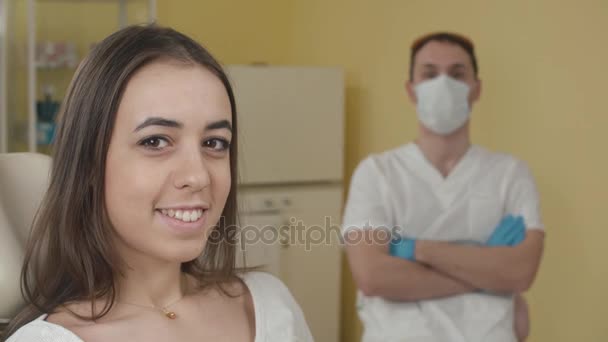 牙科诊所。快乐的女性患者着相机的镜头。在一位牙医的背景。广告的概念 — 图库视频影像