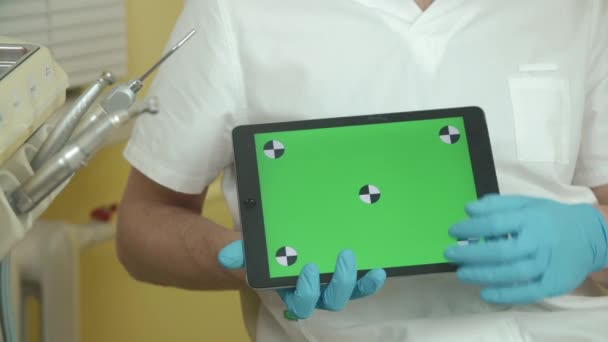 Dentista segura um tablet com uma tela verde para o seu conteúdo — Vídeo de Stock