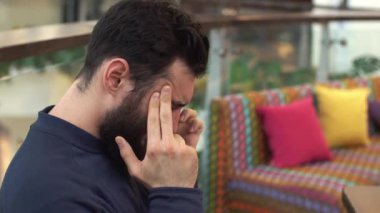 Büyük bir baş ağrısı olan genç adam. Alışveriş merkezinde bir sandalyede oturuyor