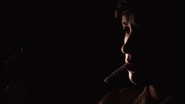 Giovane donna che cerca di accendere una sigaretta usando un fiammifero. Lei non può accendere la sigaretta, sfondo nero — Video Stock
