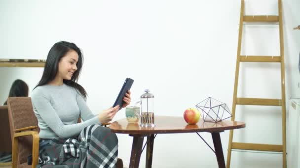 Krásná dívka pomocí tabletu a sedět na pohodlné židli doma — Stock video