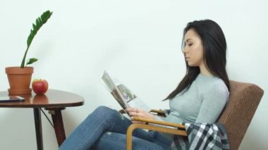 Evde rahat bir sandalyede oturuyor ve parlak dergi okuma güzel kız
