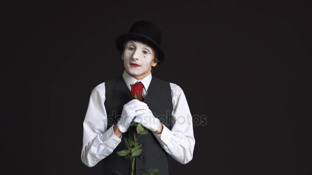 Hombre mimo con una rosa roja sobre un fondo negro. Huele la flor y sueña con una cita con una mujer. — Vídeos de Stock