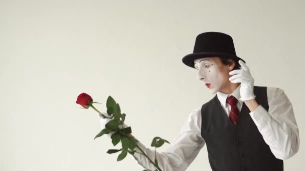 Uomo mimo con una rosa rossa su sfondo bianco. Gioca con un fiore e lo dà a qualcuno — Video Stock